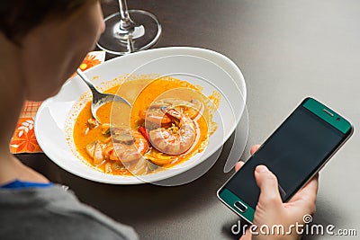 Red hot spicy prawn soup with woman hand and cellphone Stock Photo