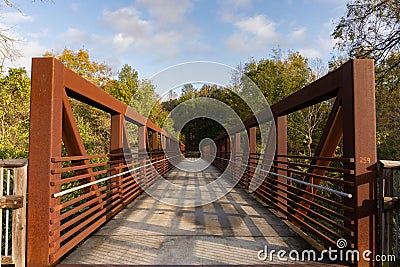 A red iron pedestrian and bicycle bridge surrounded by trees crosses over a river on the Neuse River Greenway in Raleigh, North Stock Photo