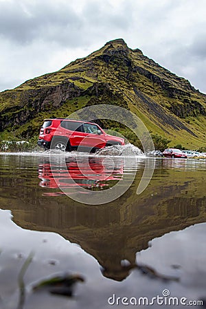 Red jeep crossing the water with a magnificent mountain in the reflection, Vik, Iceland Editorial Stock Photo