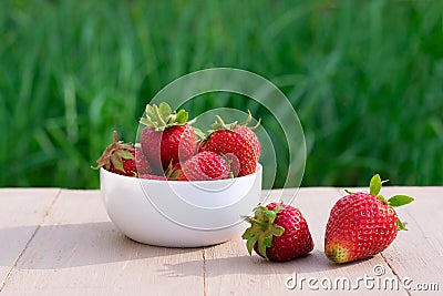 Red juicy strawberries in white bowl on blurred green background with bokeh effect Stock Photo