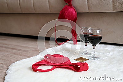 Red lace panties, bra, condom and two wine glasses on the fur rug on a floor near sofa Stock Photo