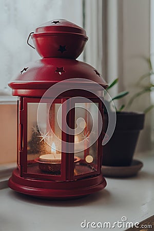 Red lamp candle holder with a lit candle on a windowsill at home Stock Photo