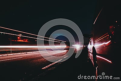 Red lights of a fast approaching car in a street on the countryside in a blue dark sky night with the moon out Stock Photo