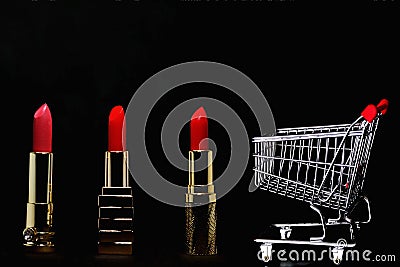 Red lipstick, gold bars and shopping cart isolated on black background with copy space Stock Photo