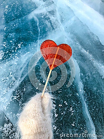 Red lollipop in the shape of a heart holds a hand in a mitten ag Stock Photo