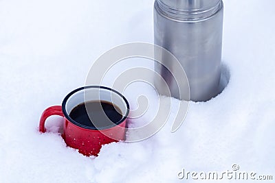 Red metal cup with coffee poured from a thermos on pure white snow in the forest while walking Stock Photo