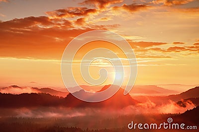 Red misty daybreak. Foggy autumn morning in a beautiful hills. Peaks of hills are sticking out from rich colorful clouds. Stock Photo