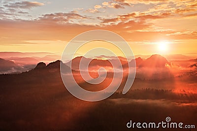 Red misty daybreak. Foggy autumn morning in a beautiful hills. Peaks of hills are sticking out from rich colorful clouds. Stock Photo