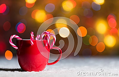 Red mug with candy canes in snow with defocussed fairy lights, bokeh in the background, Festive Christmas background Stock Photo