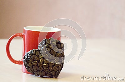 Red mug stands on the table, near the mug the heart shape of coffee beans, a symbol of love Stock Photo