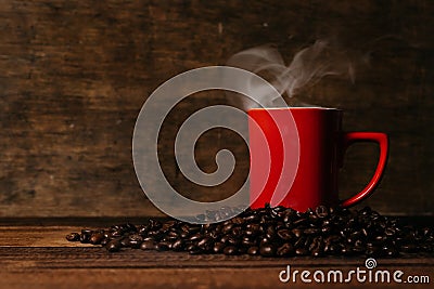 red mug with steam on a pile of fresh roasted coffee beans over wooden table Stock Photo