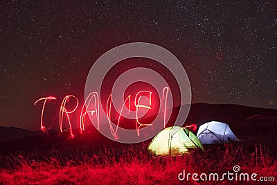 Red neon travel word. Two iluminated tents under stars at mountains at night Stock Photo