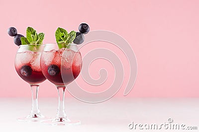 Red north homemade liquors in two wineglasses with ice cubes, blueberry, green mint on soft pastel pink background and white wood Stock Photo