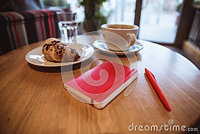 A red note and red pen is on the table in a cafe, a cup of coffee and a croissant on background Stock Photo