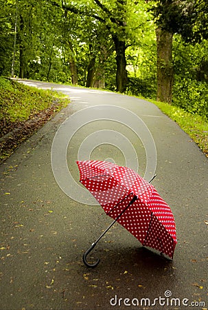 Red open umbrella lying on road among trees in nature Stock Photo