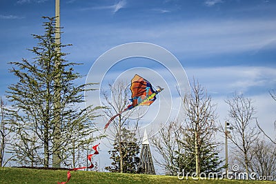 Red and orange dragon kite with long tail flying in park with pretty sky and bare trees in the background Stock Photo