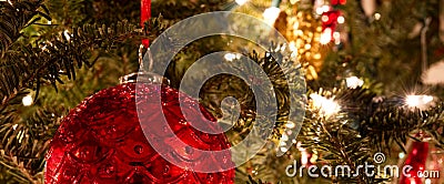 A red ball ornament hanging on a lit Christmas tree. Stock Photo