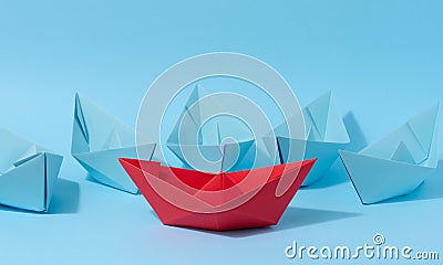 A red paper boat stands in front of a group of blue paper boats, a confrontation Stock Photo