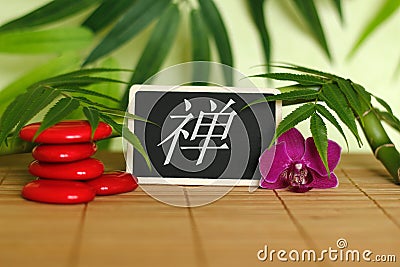 Red pebbles arranged in Zen lifestyle with an orchid, a lighted candle, a bamboo branch and foliage with the message zen on the sl Stock Photo