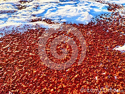 Red pebbles or rubberized textured material and white snow on it. Background, texture, frame, copy space. Contrast of Stock Photo