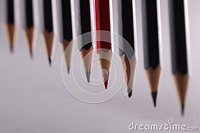 Red pencil stands out from crowd of many identical black pencils Stock Photo