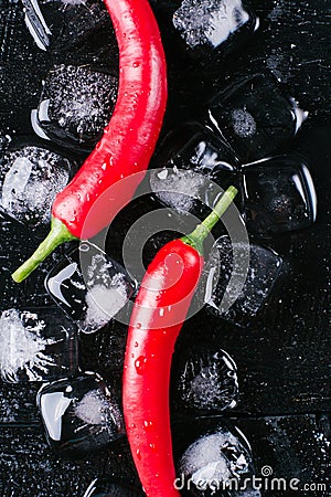 Red pepper and ice on a black wood background, fresh hot food on vintage table, freeze cold cube ice, mockup top view Stock Photo