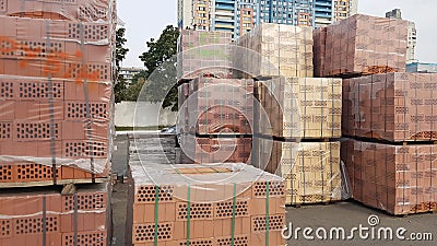 Red perforated bricks with rectangular holes on wooden pallets in an open-air warehouse ready for sale. New bricks on pallets at a Stock Photo