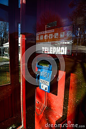 A red phone booth, inside there is a blue push-button phone with instructions to use it, taken through the glass from the outside Editorial Stock Photo