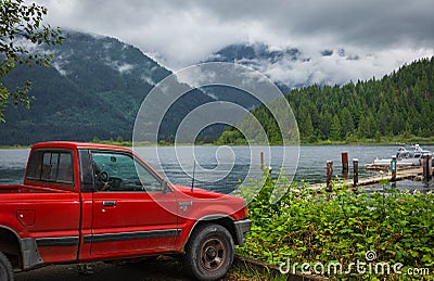 Red pickup truck parked on a lakeside with mountains in background on early moody morning. Beautiful natural landscape Editorial Stock Photo
