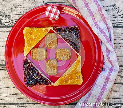 A red plate is decorated with a square made of triangular slices of bread on which fruit jam has been spread Stock Photo