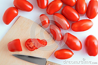 Red plum variety tomatoes on a wooden cutting board with a knife on a white background. Stock Photo