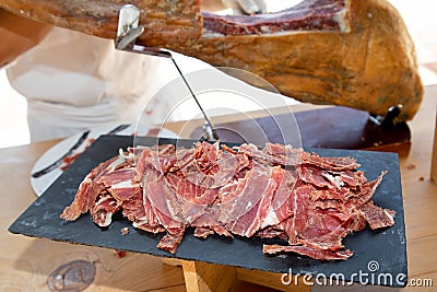 red pork cured ham cut by hand chef professional cutter carving slices from whole bone in serrano hams Stock Photo