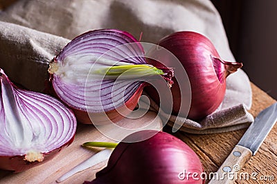 Red or purple onion cut in half, green germs, wood breadboard, linen towel, knife, kitchen table by window Stock Photo