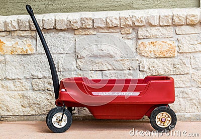 Red Radio Flyer wagon against a stone wall Editorial Stock Photo