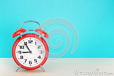 Red retro alarm clock with five minutes to nine o`clock, on wooden table on a blue background Stock Photo