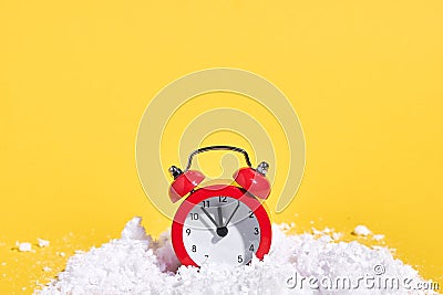 Red retro alarm clock with snow on yellow background. Creative Christmas or New year concept. Stock Photo