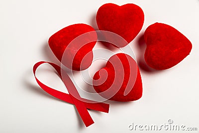 Red ribbon is near the four red heart on the white background/table. World AIDS Day Stock Photo