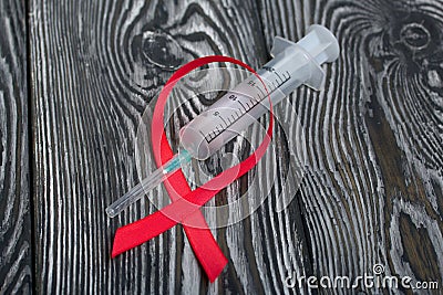 Red Ribbon Symbol for World AIDS Day. On top of it lies a medical syringe. Lies on black pine boards Stock Photo