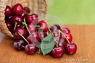 Red Ripe Cherries spilling from basket on a wood table Stock Photo