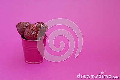 Red ripe fresh strawberries on a pink background lies in a pink bucket. spilled from a bucket of ripe strawberries. Stock Photo