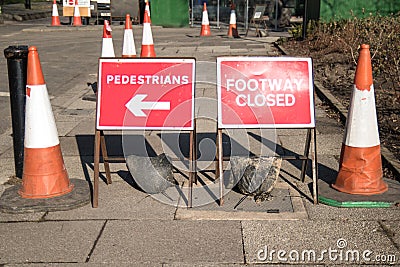 Red road traffic signs saying Footway Closed and directing Pedestrians with an arrow. Traffic cones used to block pavement Editorial Stock Photo