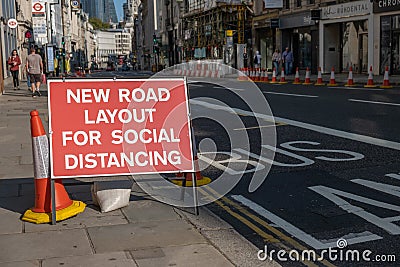 A red roadwork sign next to a bus lane saying new road layout for social distancing with a London street in the background Editorial Stock Photo