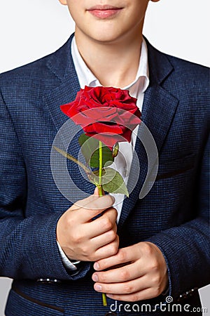 Red rose in the hands of a teenager. The boy is dressed in a blue suit and white shirt Stock Photo