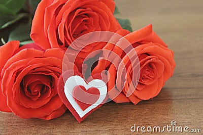 Red roses in a bouguet with a souvenir in the shape of a heart red and white color s lie on a wooden table brown. Macro. Stock Photo