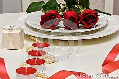 Red Roses on a white plate, candles and giftbox. Romantic composition for Valentine`s Day, Anniversary, Events. Place Stock Photo