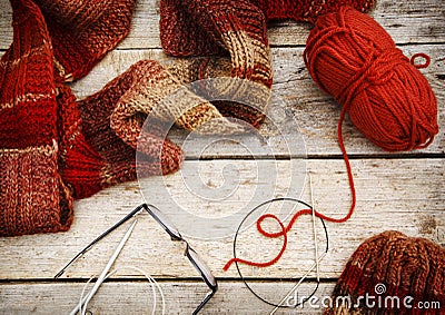 Red scarf and hat near knitting needles and woolen threads on wooden background. Winter and autumn warm clothing, top view. Stock Photo