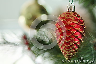 Red shining pine acorn cone hanging on a Christmas tree with blur bokeh background. New Year decoration prop. Stock Photo