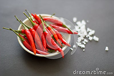 Red small spicy peppers in a green bowl with salt crystals nearby on a black background.Close-up, top view Stock Photo