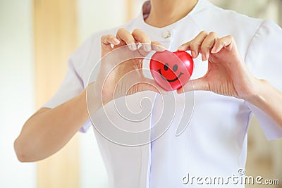 Red smiling heart held by female nurse`s both hands, representing giving effort high quality service mind to patient. Profession Stock Photo