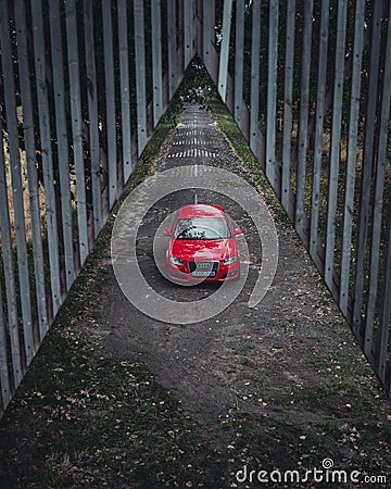 red sports car parked on a dirt path next to tall wooden fence Editorial Stock Photo